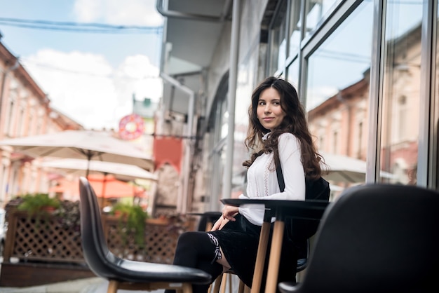 Menina linda sentada em uma cafeteria esperando seu cappuccino, horário de verão