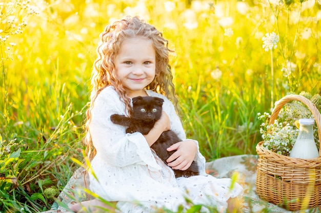 Menina linda sentada no gramado no verão com um gatinho preto