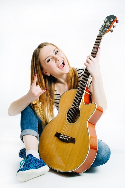 Menina linda vestindo jeans e uma camiseta listrada com um violão em um fundo branco