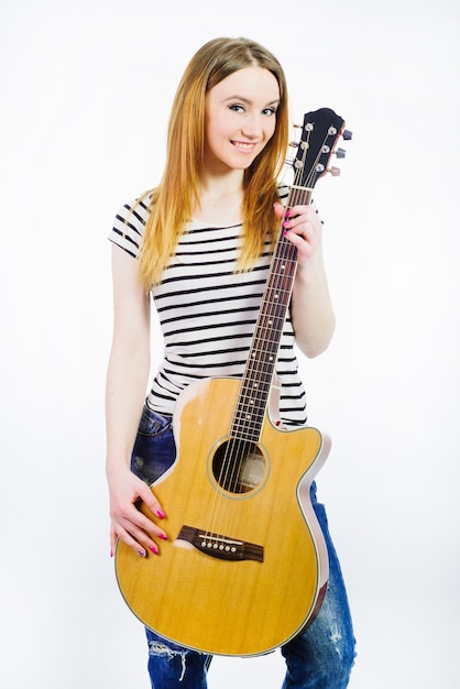 Menina linda vestindo jeans e uma camiseta listrada com um violão em um fundo branco