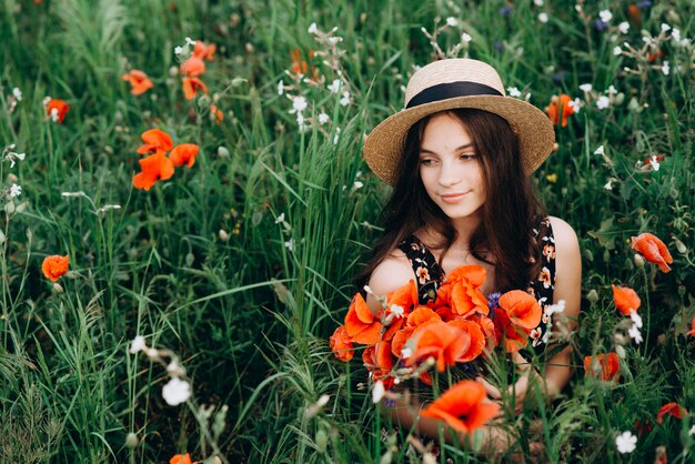 Menina livre linda em um chapéu em um campo de verão de papoilas vermelhas com um buquê