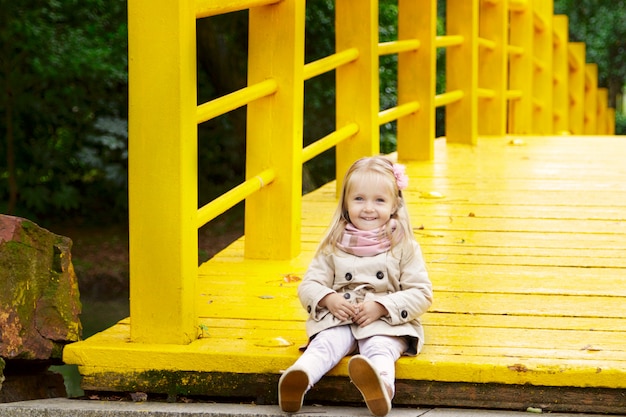Menina llittle elegante em uma ponte amarela no parque