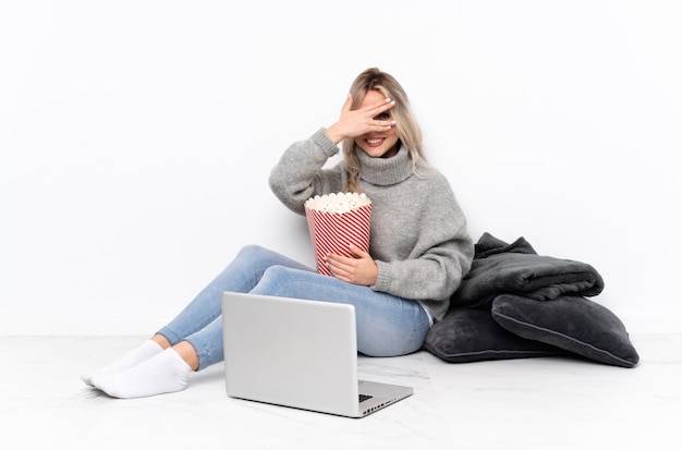 Menina loira adolescente comendo pipoca enquanto assiste a um filme no laptop