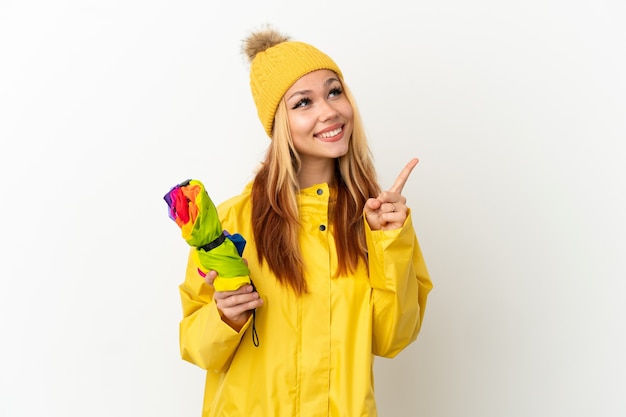 Menina loira adolescente vestindo um casaco à prova de chuva sobre um fundo branco isolado apontando uma ótima ideia