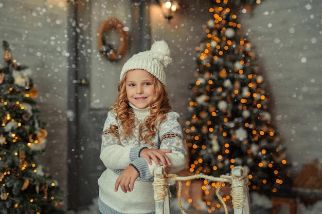 menina loira alegre com um chapéu no fundo de uma casa de madeira no inverno