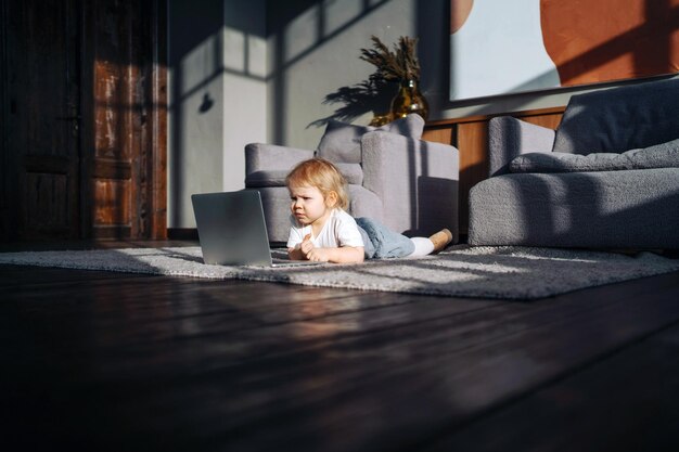 Menina loira assistindo desenhos em um laptop deitado no chão macio