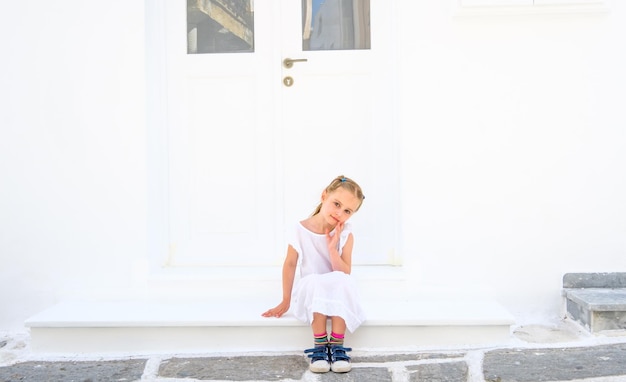 Menina loira bonita em um vestido branco sentado ao ar livre perto da casa branca