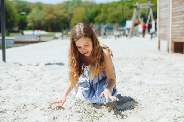 Menina loira bonitinha brincando na areia no verão de praia