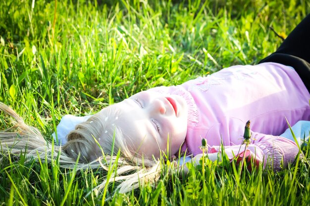 Menina loira bonitinha com pétalas brancas de cerejeira no cabelo dela deitado no prado verde no parque primavera
