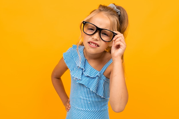 menina loira bonitinha de óculos estrabismo em uma parede laranja