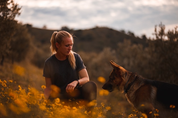 Menina loira brincando com o cão pastor alemão em um campo de flores amarelas