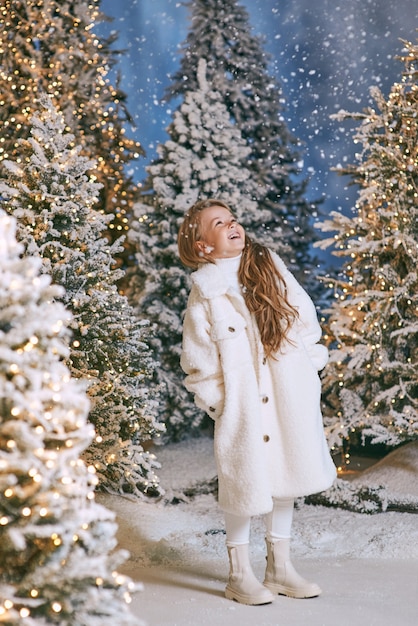 menina loira caucasiana com casaco de pele eco branco andando na floresta de Natal de inverno com luzes