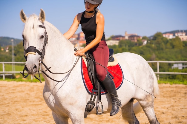 Menina loira caucasiana montando um cavalo branco, vestida de cavaleiro preto com chapéu de segurança