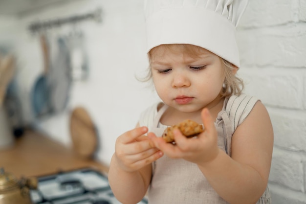 Menina loira chef brincando na cozinha come biscoitos frescos e sobremesas