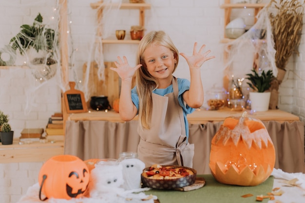 menina loira com avental na cozinha decorada com abóboras para o Halloween preparando uma torta de focaccia