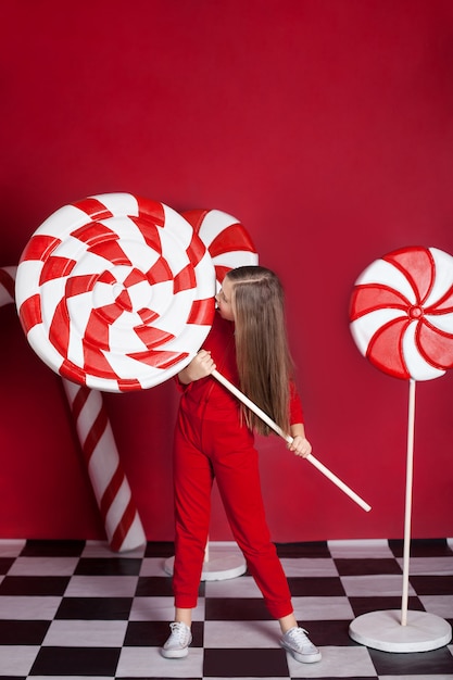 Menina loira com enormes doces de Natal em uma parede vermelha isolada.