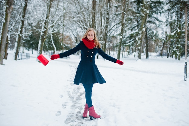 Menina loira com lenço vermelho e casaco andando no parque num dia de inverno.