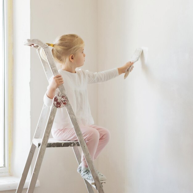 menina loira com rolo de pintura de parede durante a renovação da casa