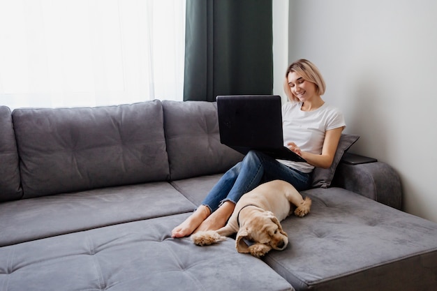 Menina loira com um cachorro sentado no sofá com um laptop espaço para texto