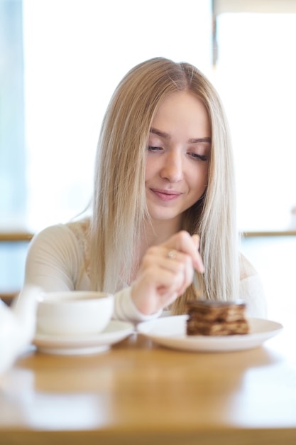 Menina loira comendo bolo no café