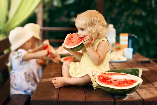 Menina loira comendo uma melancia suculenta no jardim. as crianças comem frutas na rua. comida saudável para as crianças. jardinagem da criança.