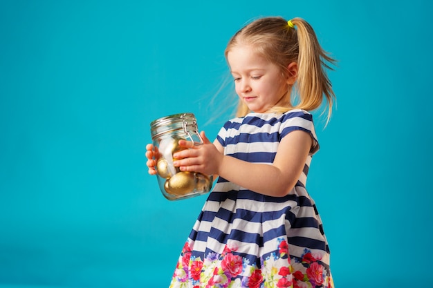 Menina loira criança com frasco de vidro cheio de ovos pintados de ouro para a Páscoa