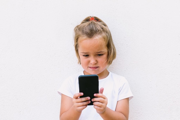 Menina loira de camiseta branca, olhando para o celular, virado, tirando uma foto