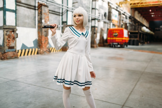 Menina loira de estilo anime bonita com espada posa na fábrica abandonada. Moda cosplay, cultura asiática, boneca com lâmina, mulher bonita com maquiagem