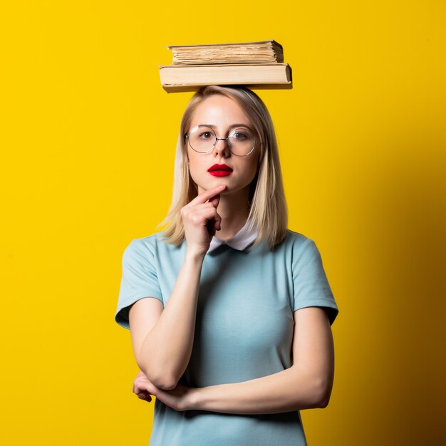 Menina loira de vestido azul e óculos com livros no espaço amarelo