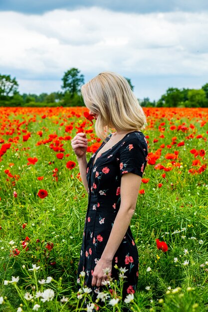 Menina loira de vestido bonito no campo de papoulas no horário de verão