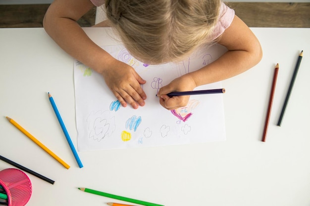 Menina loira desenha com lápis de cor sentados à mesa Vista superior plana