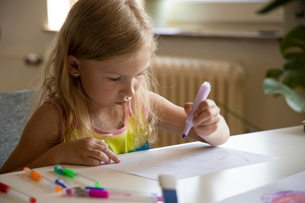 Foto menina loira desenha enquanto está sentada à mesa