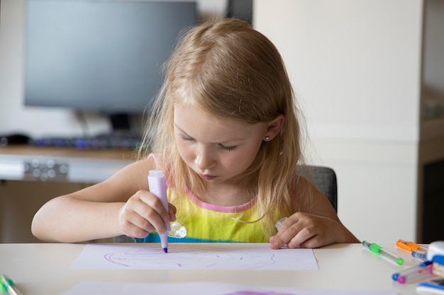 Foto menina loira desenha enquanto está sentada à mesa