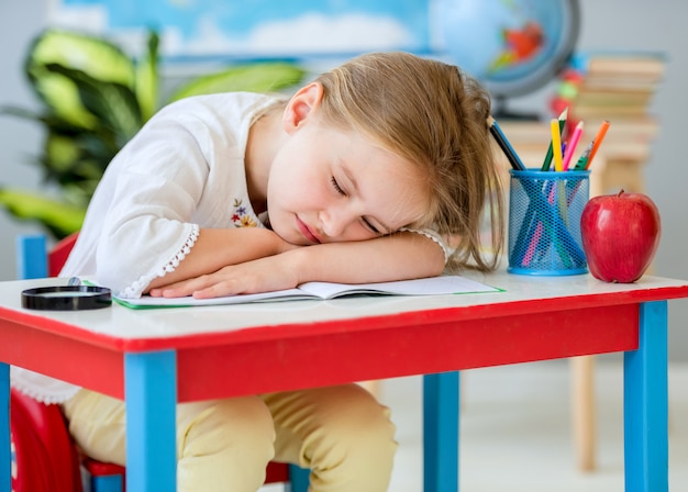 Menina loira e bonita dormindo na mesa branco-vermelha na sala de aula