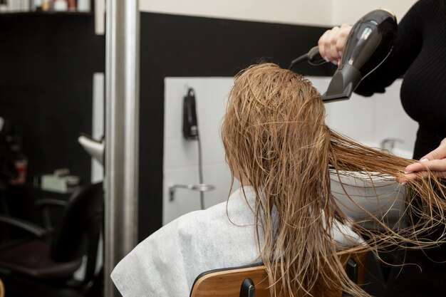 Menina loira em um salão de beleza secar o cabelo dela. Fechar-se.