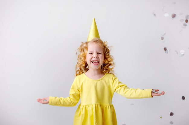 Menina loira em um vestido amarelo pega confete sorrindo feliz em fundo branco