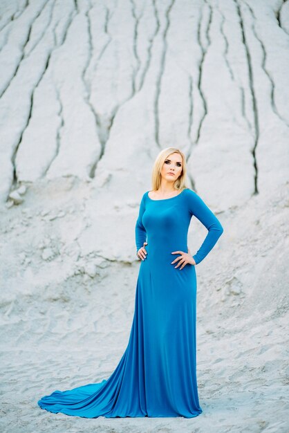 Foto menina loira em um vestido azul com olhos azuis em uma pedreira de granito contra o fundo de cascalho