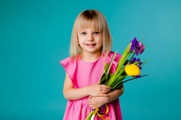 Menina loira está sorrindo em um vestido rosa e segurando um buquê de flores da primavera em um espaço azul isolar