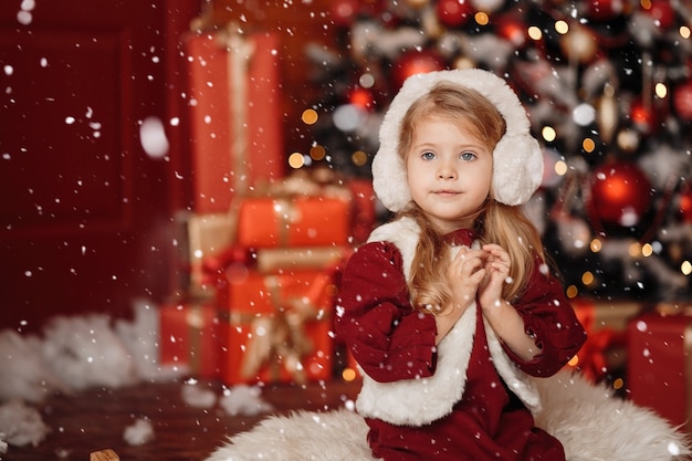 Menina loira feliz com um colete de pele e fones de ouvido, esperando pelo Natal