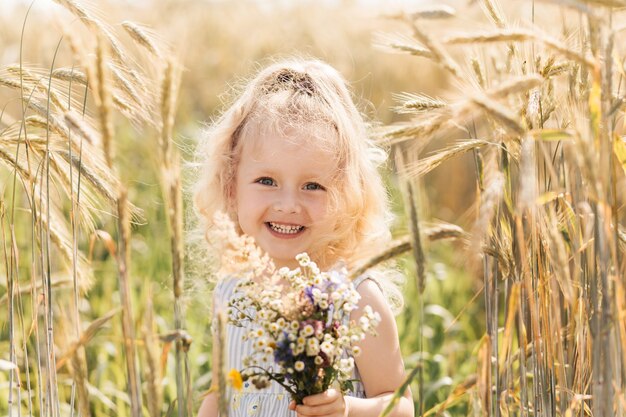 Menina loira fofa com um buquê de flores silvestres na natureza no verão