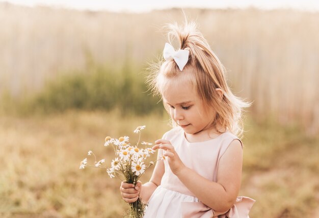 Menina loira fofa com um buquê de flores silvestres na natureza no verão