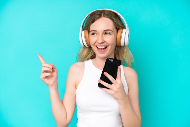 Menina loira inglesa isolada em fundo azul ouvindo música com um celular e cantando