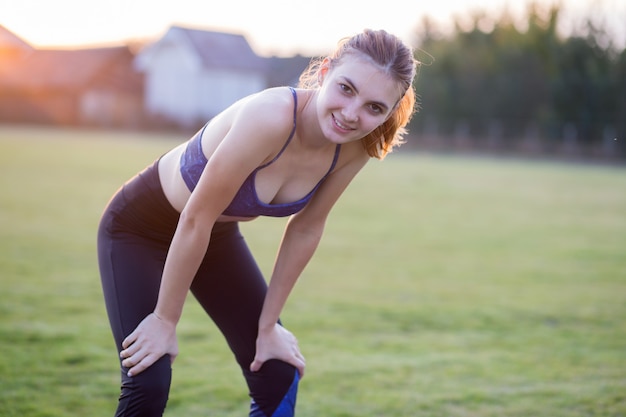 Menina loira magro pratica esportes e realiza poses de ioga na grama do verão