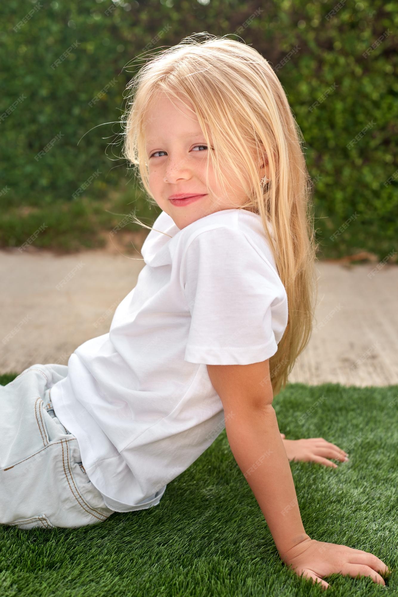 Feliz Bebê Loira Com Duas Pequenas Tranças Em Camiseta Branca E Um Kit De  Calças Jeans Sentado Sobre O Fundo Da Grama Verde Foto de Stock - Imagem de  pouco, inocência: 143643548