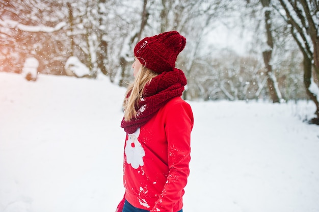 Menina loira no suéter vermelho cachecol, chapéu e papai noel posando no parque em dia de inverno.