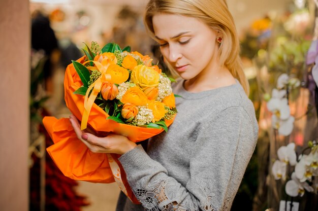 Menina loira segura um buquê de rosas e tulipas laranja