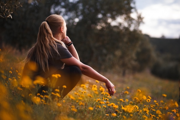 Menina loira sentada em um campo de flores amarelas