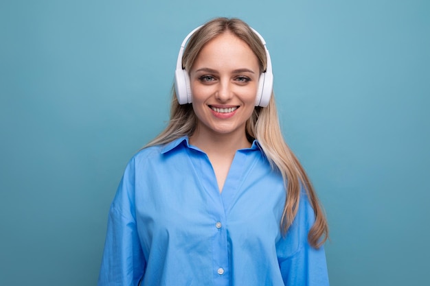 Menina loira sorridente em camisa casual ouvindo música em fones de ouvido grandes