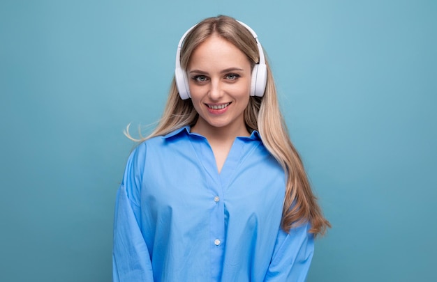 Menina loira sorridente em camisa casual ouvindo podcast em fones de ouvido grandes