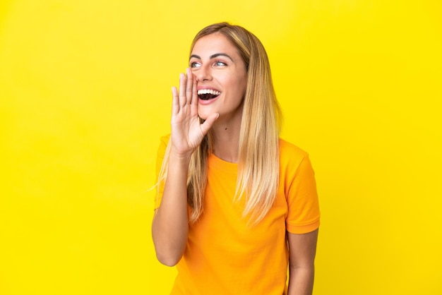 Menina loira uruguaia isolada em fundo amarelo gritando com a boca aberta para o lado